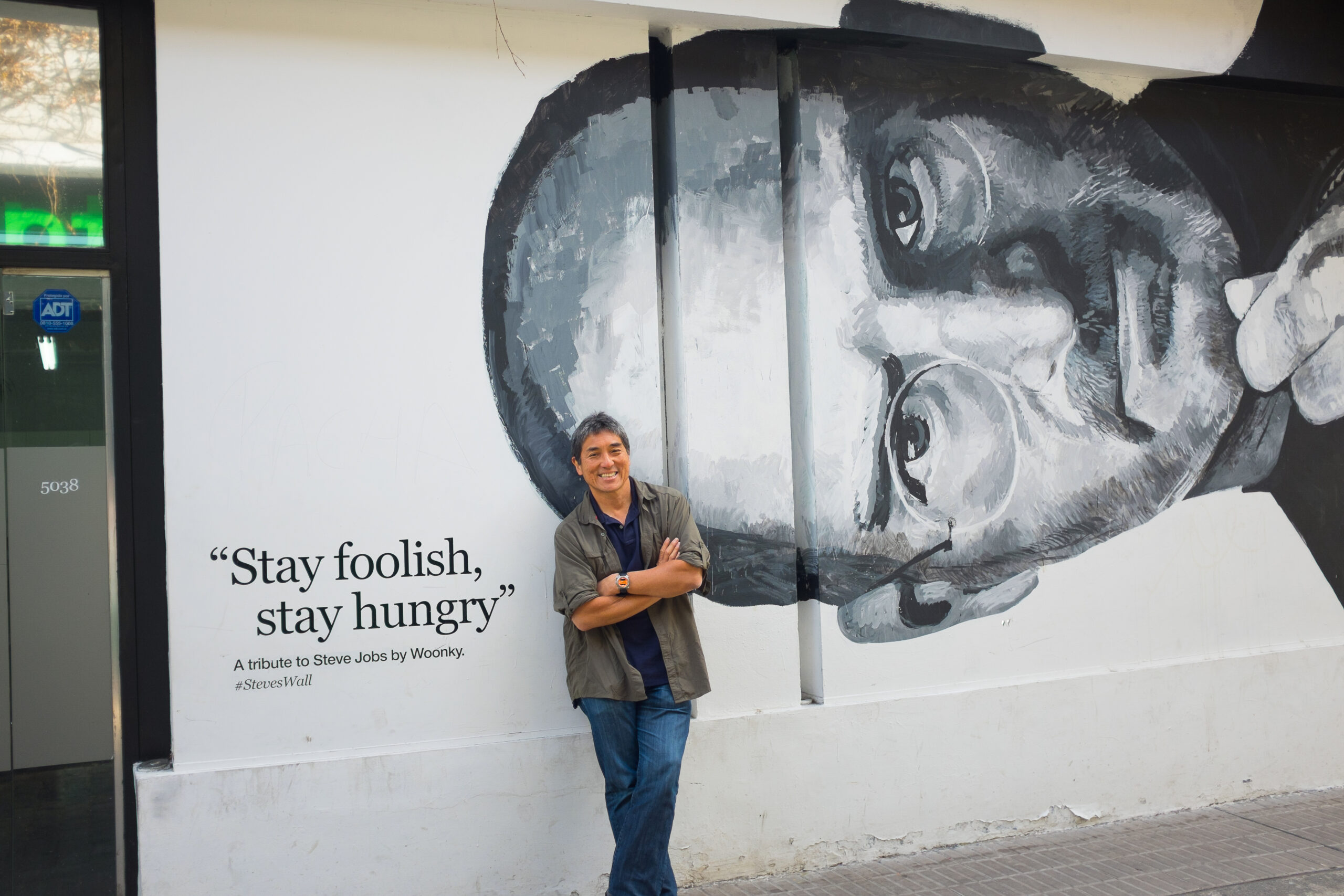 Guy Kawasaki in front of a poster of Steve Jobs saying 'stay hungry, stay foolish'